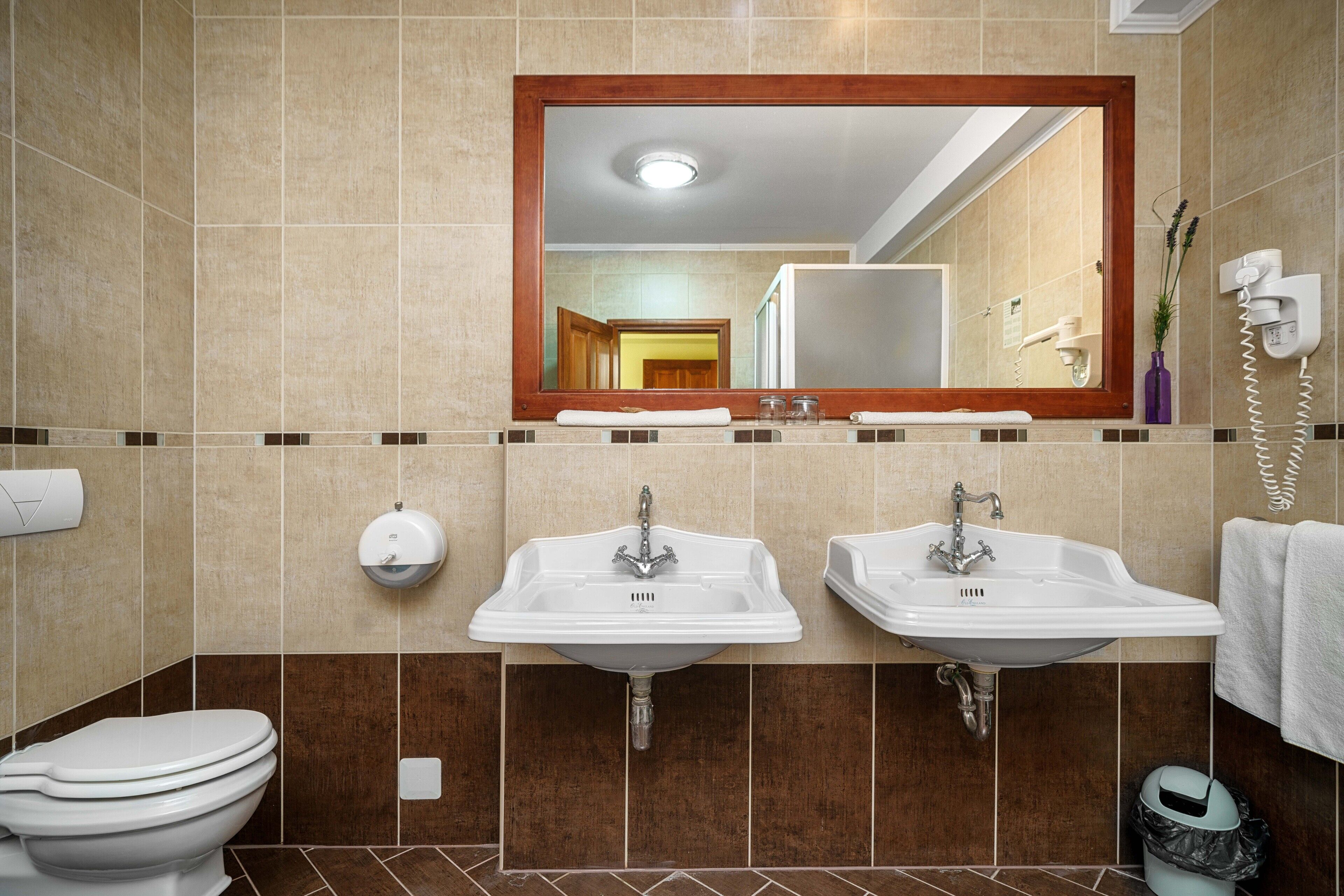 A bathroom with two sinks, a toilet, and a mirror.