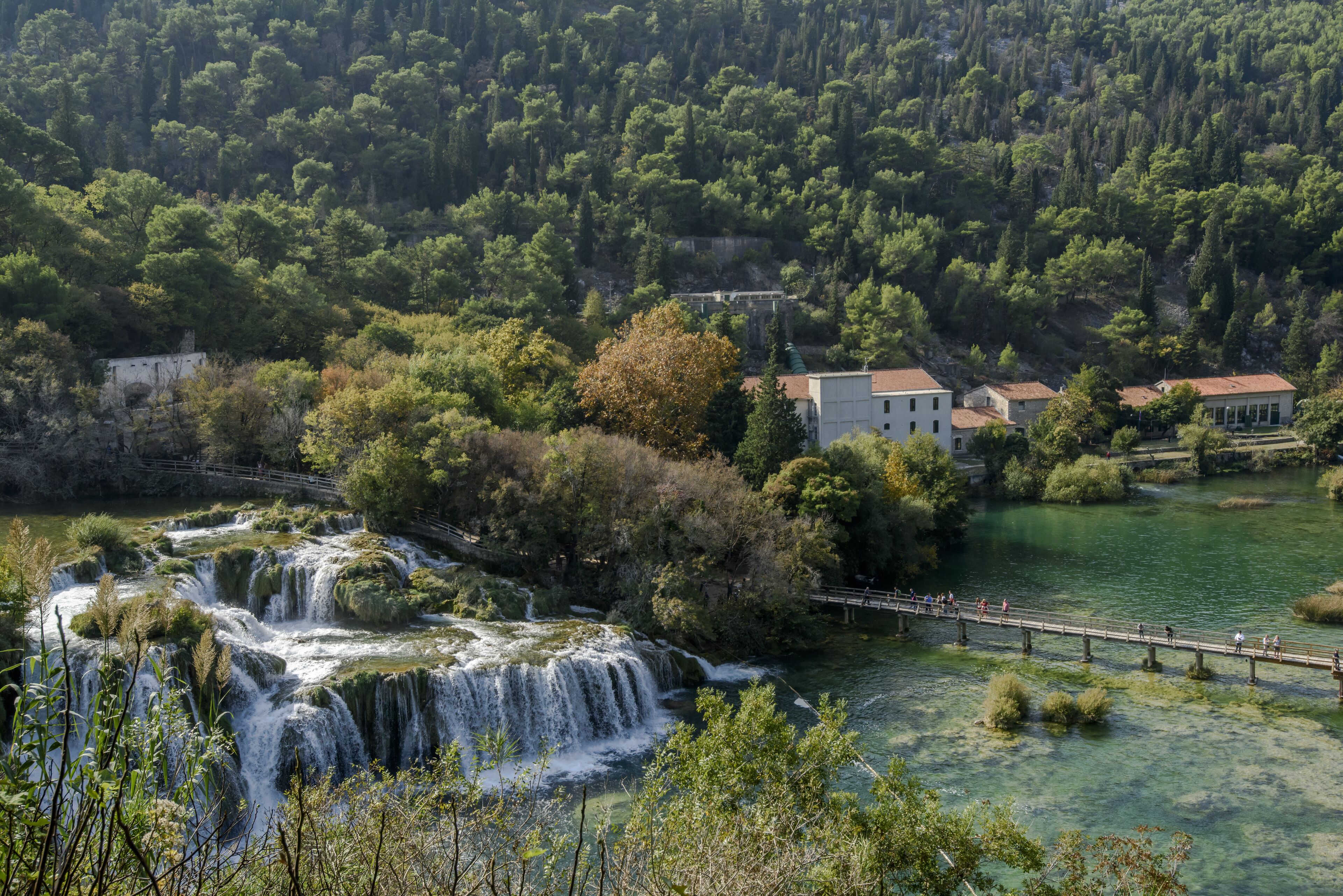Una cascada, un puente y un edificio rodeado de árboles.