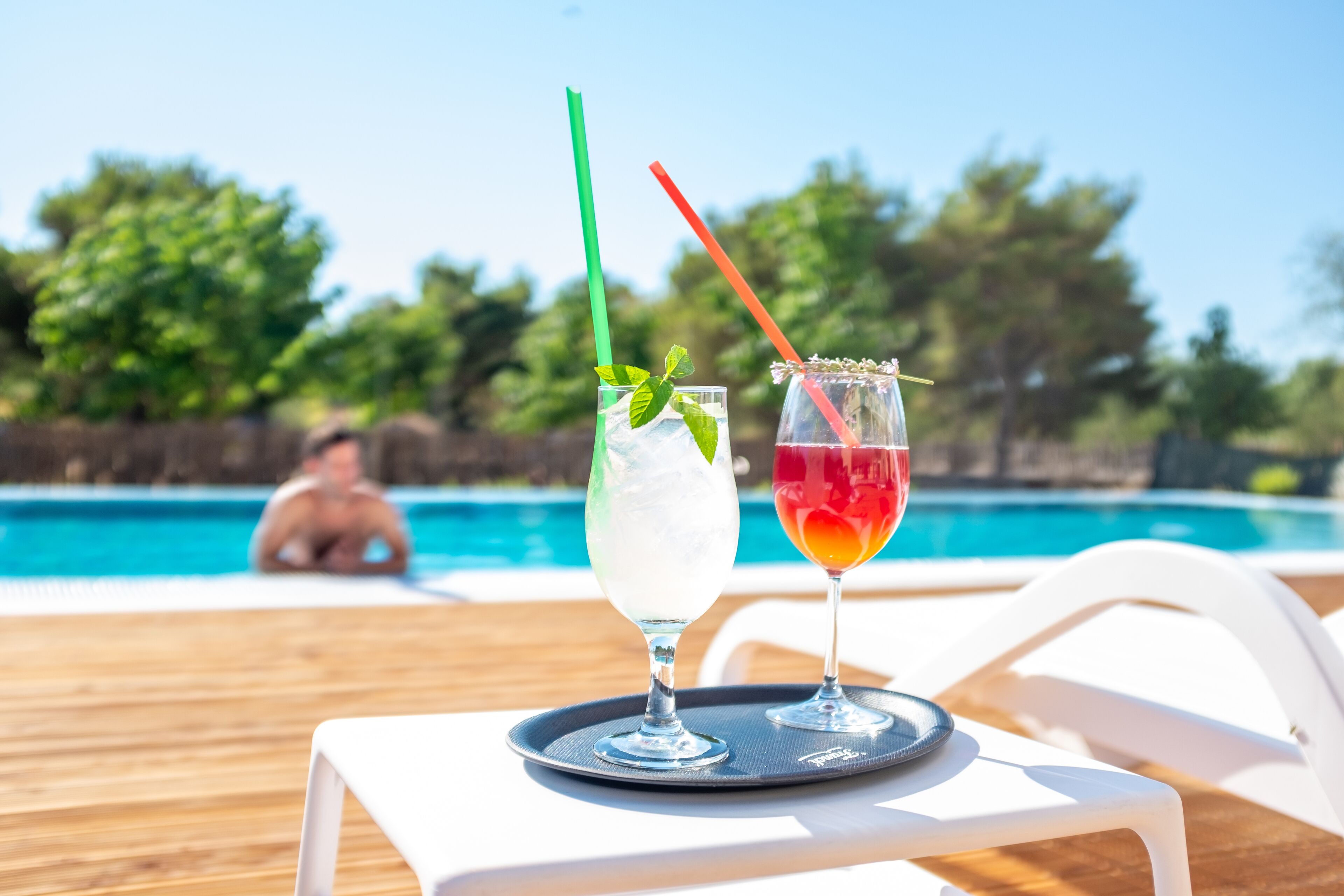Two drinks on a tray by a poolside chair.
