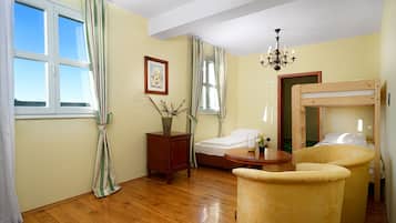 A room with a bunk bed, a wooden desk, a chair, a small table with a vase, and a chandelier.