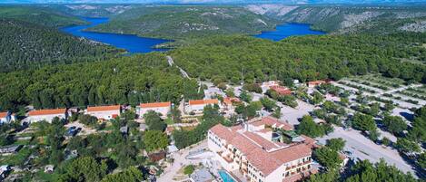 Vista aérea de um resort com vários edifícios, uma piscina e áreas arborizadas ao redor.