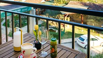 Una mesa de madera con una taza, un vaso y una botella en un balcón con vistas a una zona residencial.