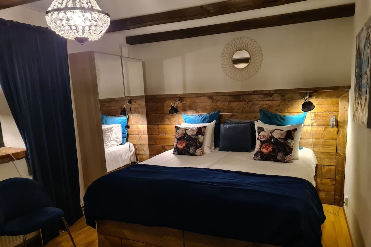 A bedroom with a wooden headboard, a large bed with floral pillows, a chandelier, and a mirror.