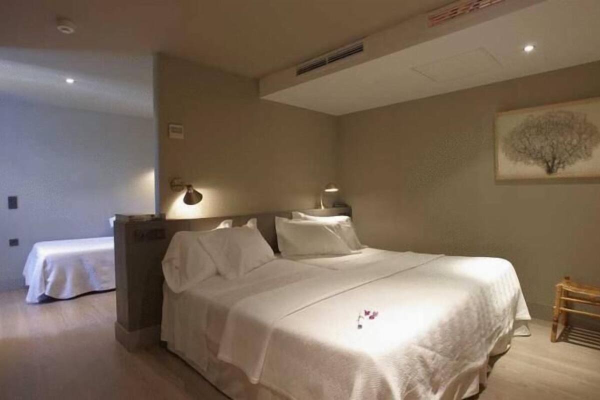 A hotel room with a large bed, bedside tables, a nightstand, a chair, and a wall-mounted lamp.