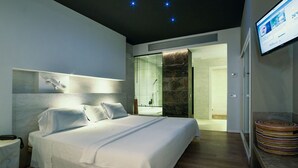 A modern hotel room with a large bed, a bedside table, a wall-mounted TV, and a bathroom with a shower and toilet. - MC San José (Nijar)