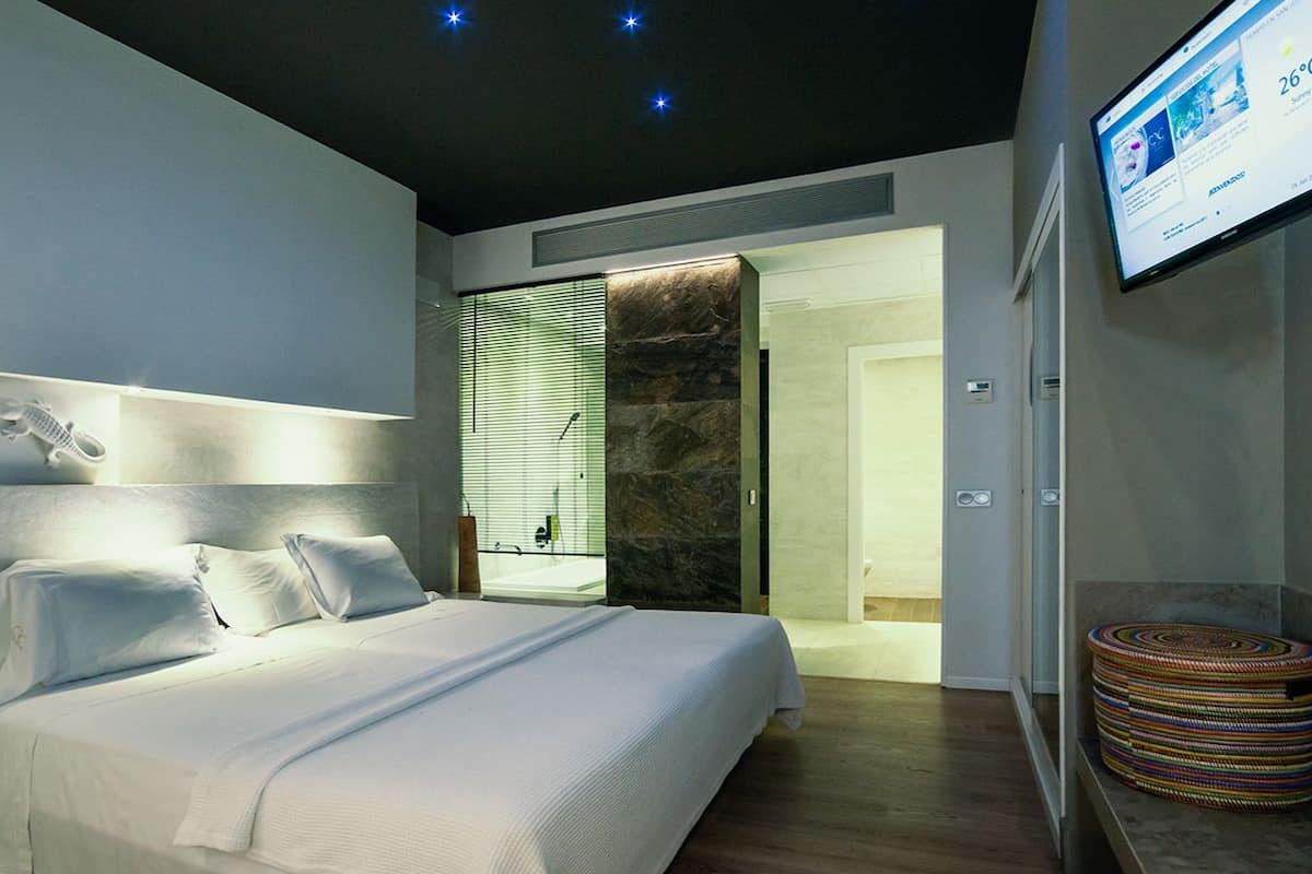 A modern hotel room with a large bed, a bedside table, a wall-mounted TV, and a bathroom with a shower and toilet.