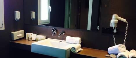 A hotel bathroom with a sink, towel dispenser, and hairdryer.