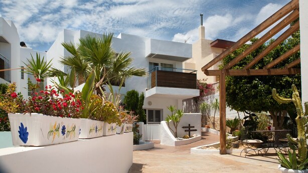 A courtyard with white buildings, a wooden pergola, and various plants. - MC San José (Nijar)