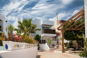 A courtyard with white buildings, a wooden pergola, and various plants.
