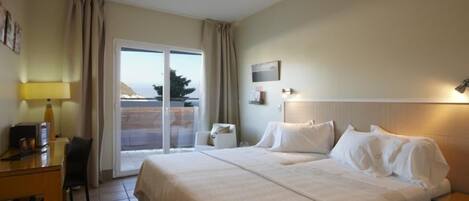 A hotel room with a large bed, a desk with a lamp, a chair, and a view of the outdoors through a sliding door.
