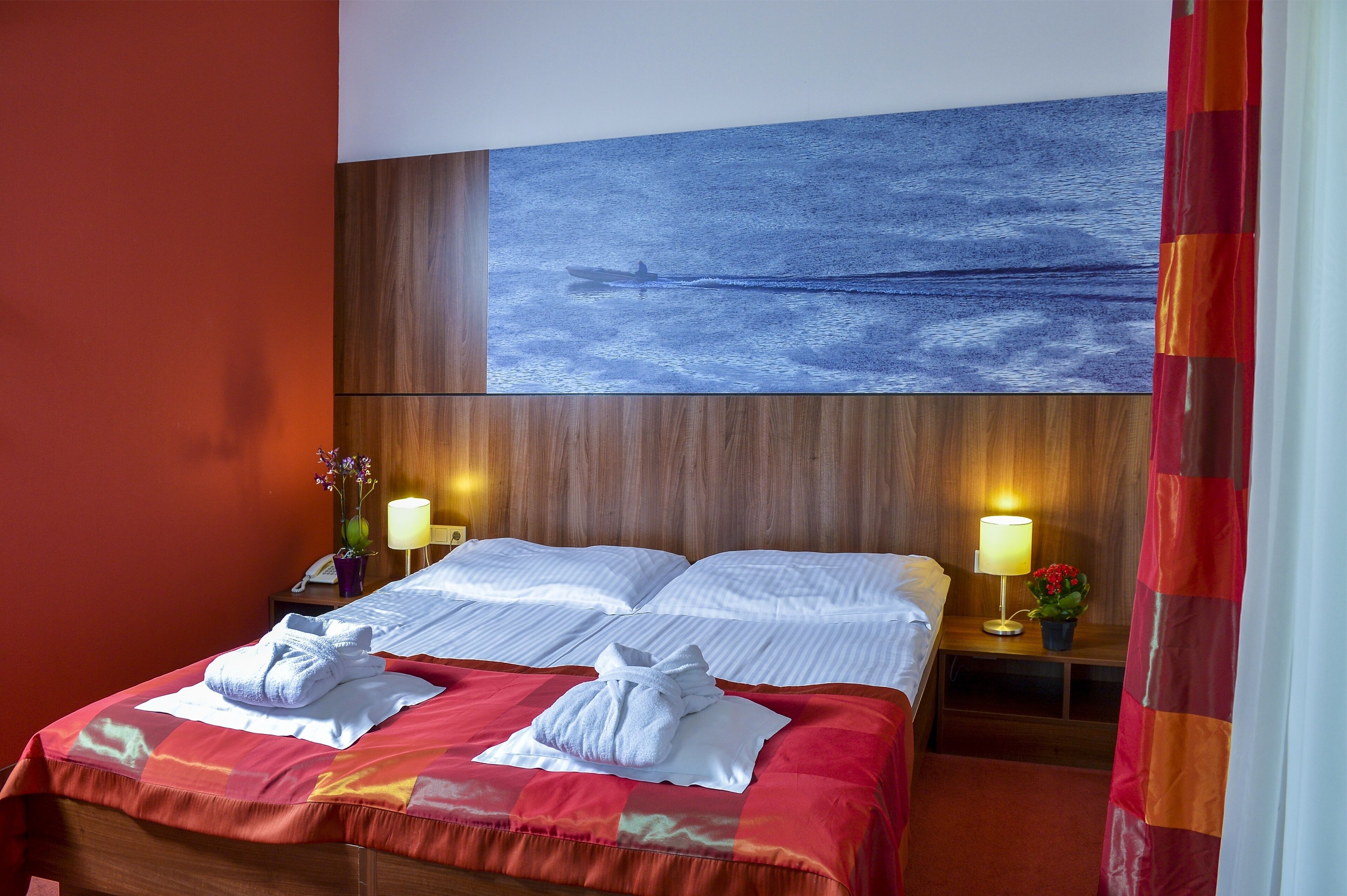 A hotel room with a large bed, two bedside tables, a nightstand, a wall-mounted painting, and a curtain.