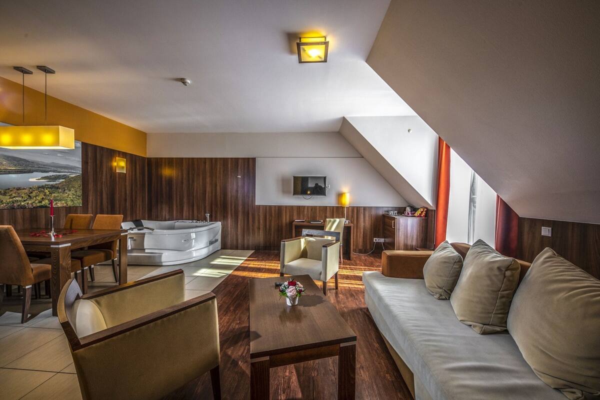 A modern hotel room with a sofa, dining table, and a TV mounted on the wall.