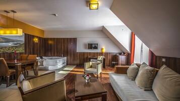 A modern hotel room with a sofa, dining table, and a TV mounted on the wall.