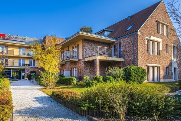 A modern hotel with a brick facade, a covered outdoor area, and a paved walkway. - Royal Club Hotel (Visegrád)