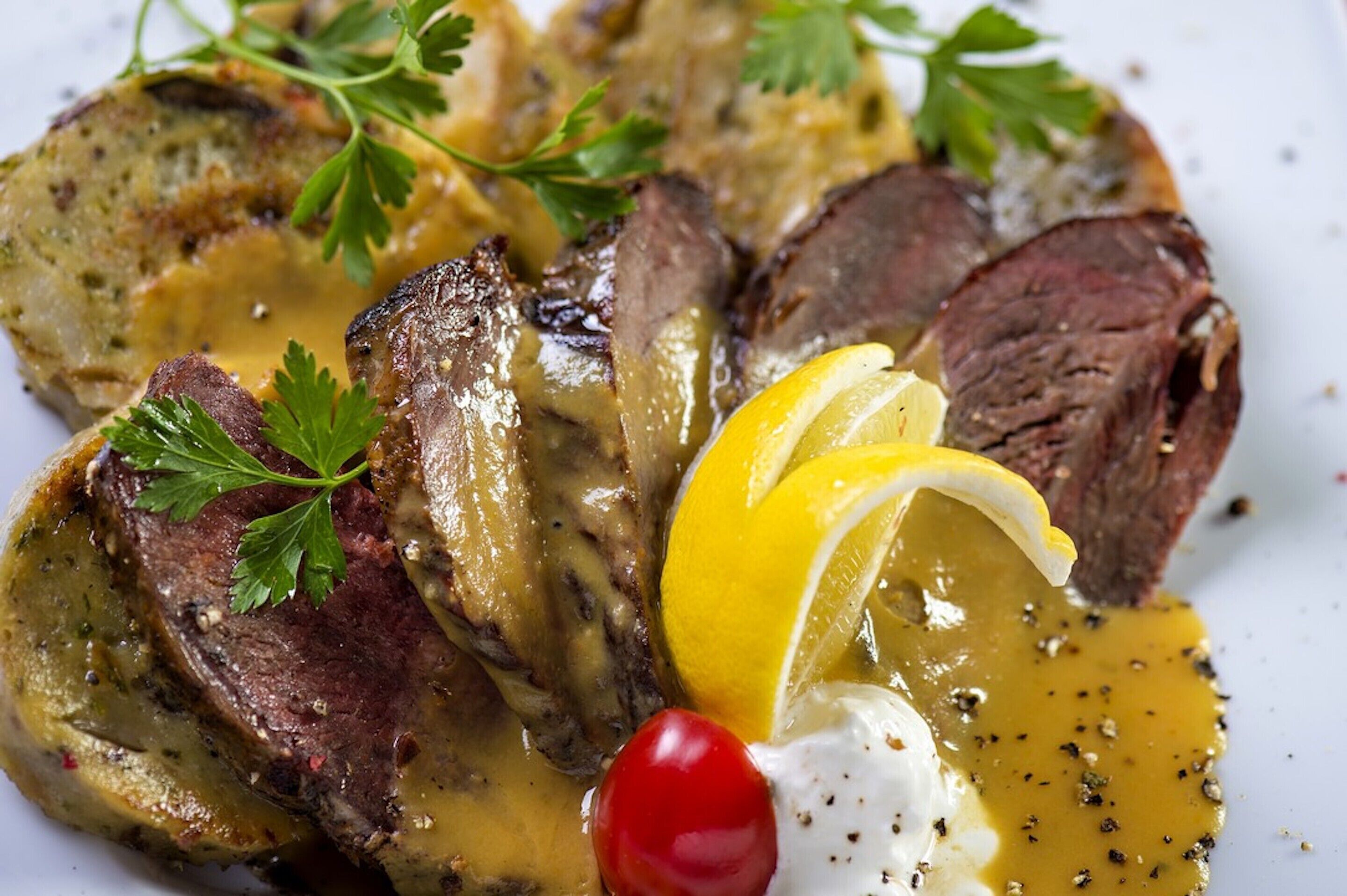Une assiette de nourriture comprenant un steak, une sauce, un citron et une garniture.