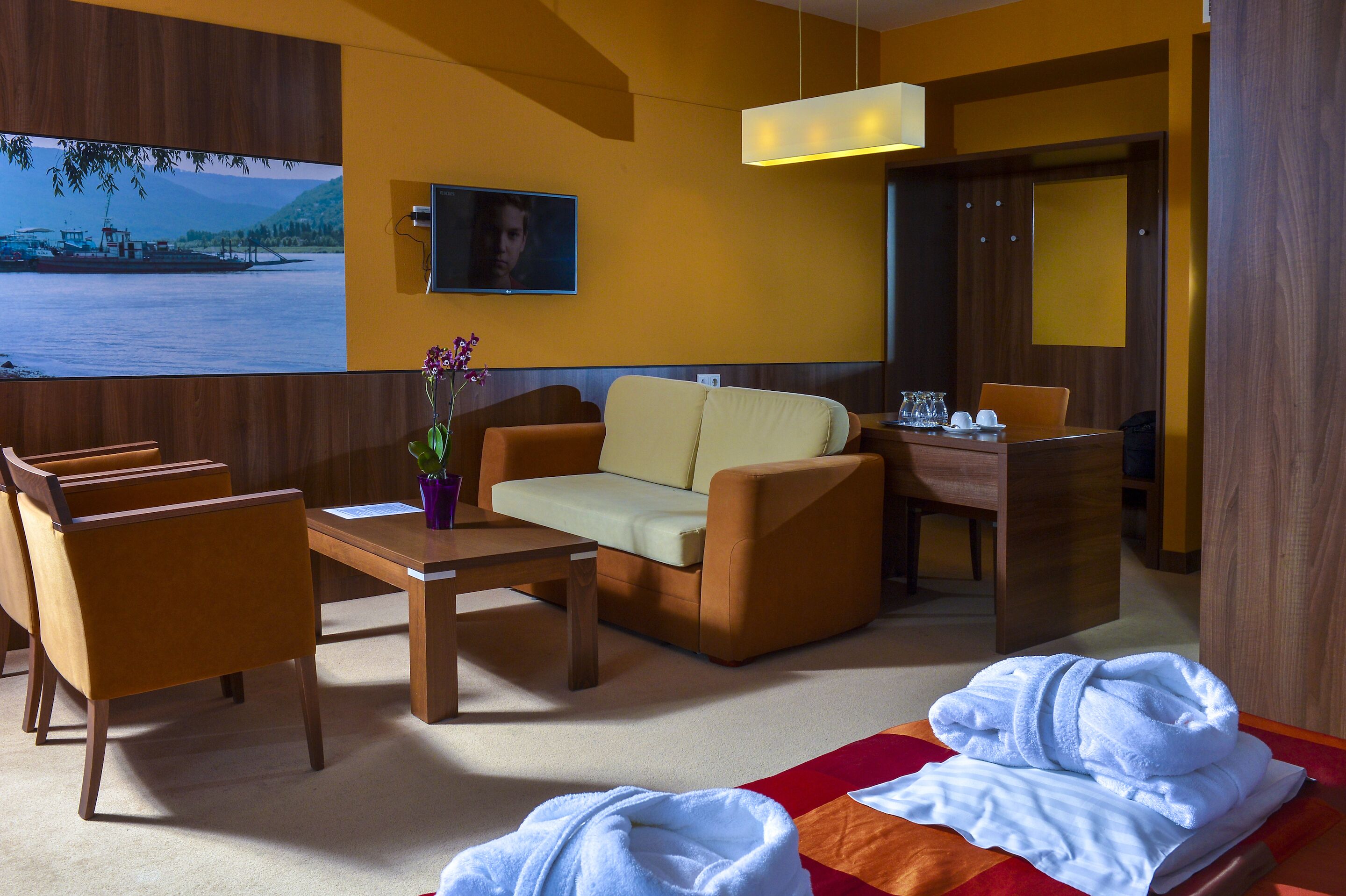 Habitación de hotel con sofá, sillas, una mesa de comedor, televisión y una cama con toallas.
