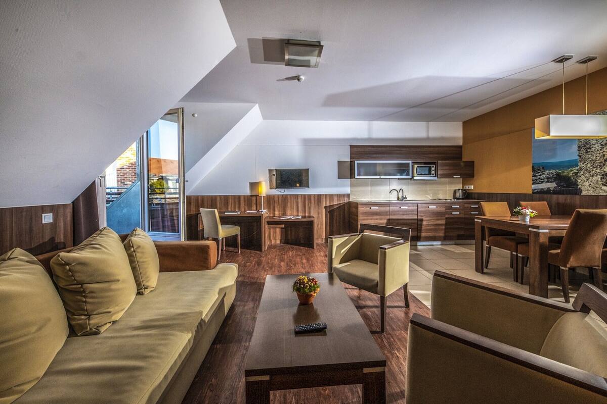 A modern living area with a sofa, coffee table, and chairs, a dining table with chairs, a kitchen area with a microwave, and a large window with a view.