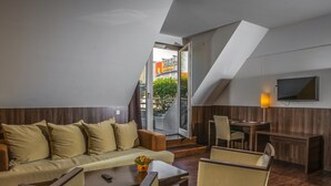 A modern hotel room with a sofa, armchairs, a dining table, and a TV. - Royal Club Hotel (Visegrád)