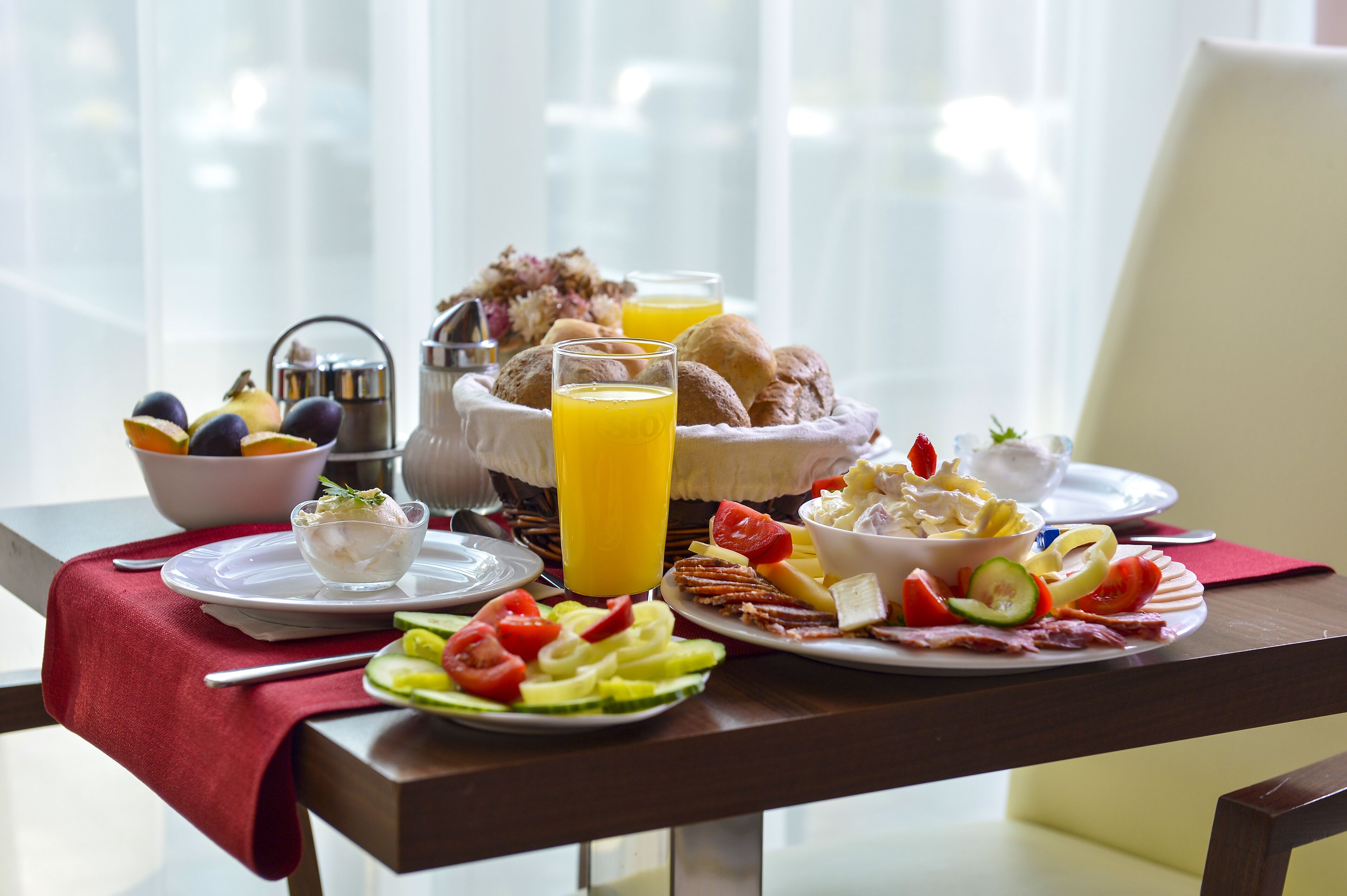 A breakfast table with plates of food, a fruit bowl, a pitcher, and a glass of orange juice.