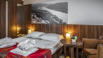 A hotel room with a large bed, two bedside tables, a small round table with a vase of flowers, and a large framed picture of a landscape on the wall.