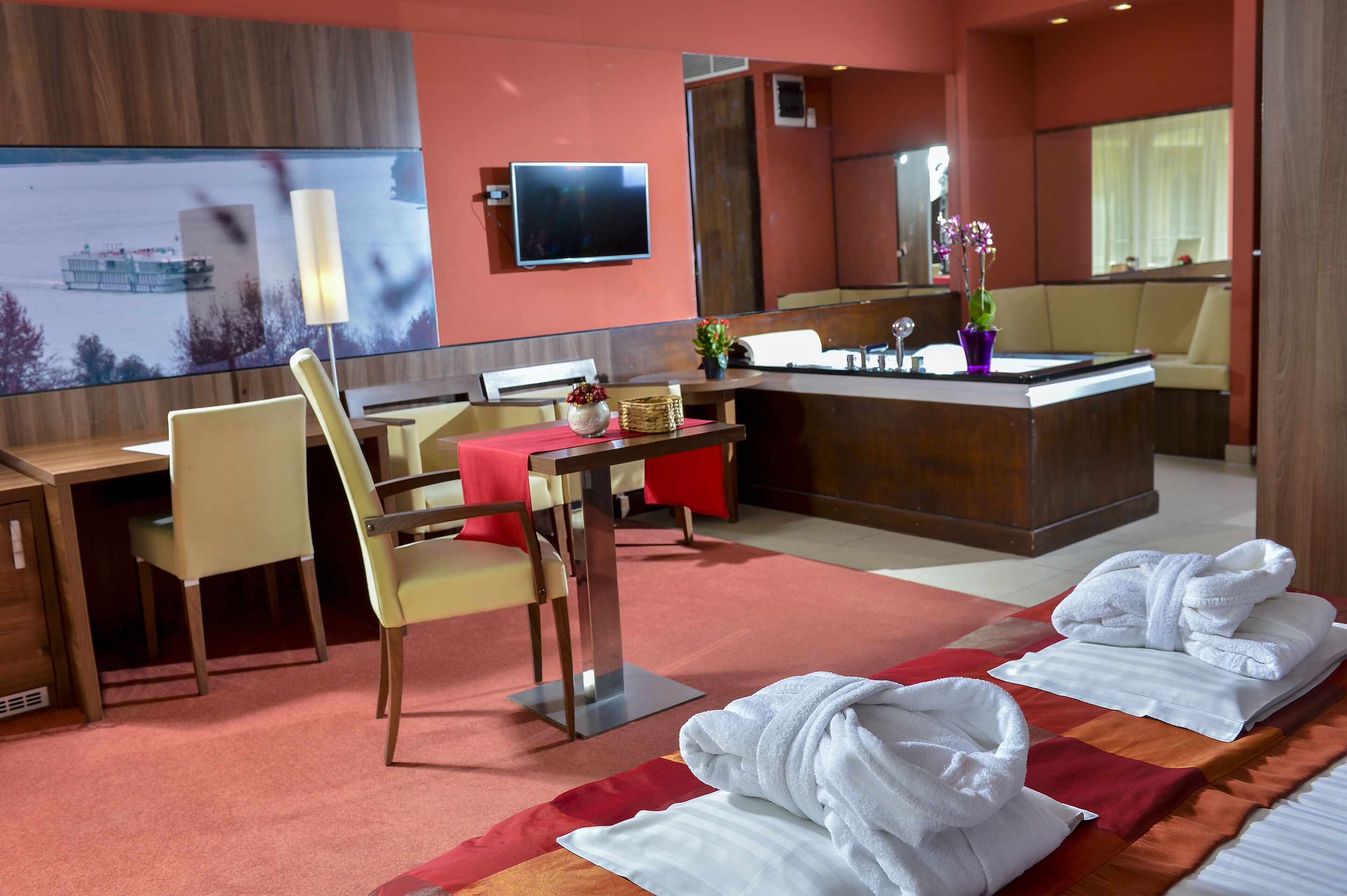 A hotel room with a desk, chairs, a TV, a mirror, and towels on the bed.