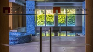 A modern interior of the Royal Club Hotel in Viségrad with a glass partition, a pool area, and a view of greenery outside. - Royal Club Hotel (Visegrád)