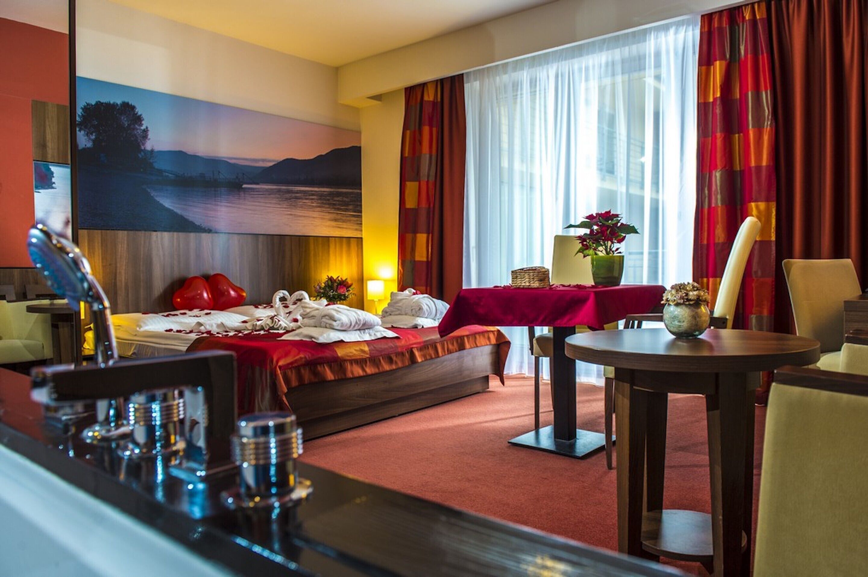 A hotel room with a bed, a dining table, a chair, a lamp, and a painting on the wall.