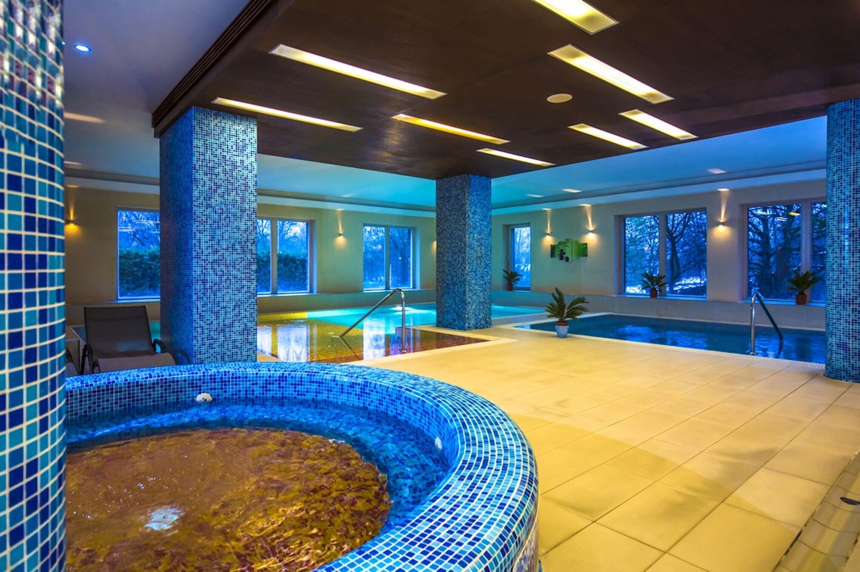 An indoor swimming pool with a mosaic-tiled wall and a hot tub area.