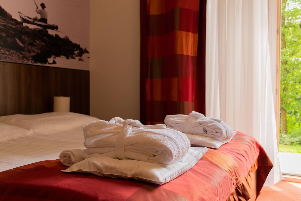 A neatly made bed with white towels and a red bedspread.