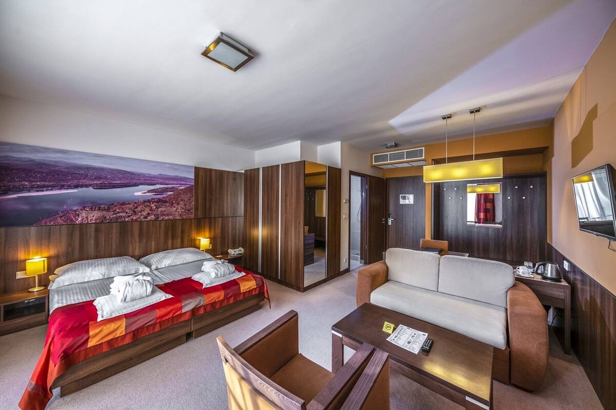 A modern hotel room with a large bed, a sofa, a small table, and a TV.
