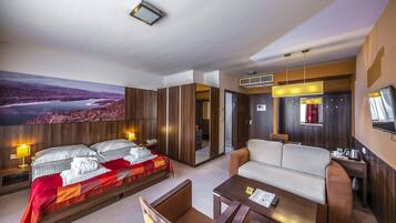 A modern hotel room with a large bed, a sofa, a small table, and a TV.