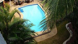 A swimming pool surrounded by palm trees and a covered patio area with outdoor furniture.