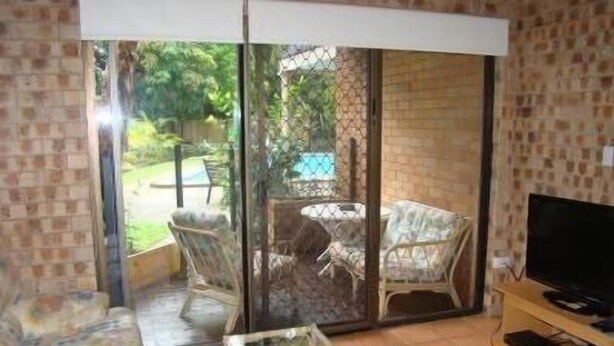 A room with a sliding glass door leading to a patio area with outdoor furniture and a TV on a wooden stand.