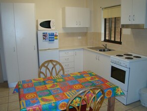 Una pequeña cocina con microondas, estufa, pileta y una mesa con mantel colorido.