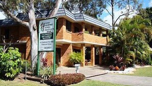 A two-story building with a balcony, surrounded by trees and plants.