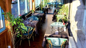 An outdoor dining area with tables and chairs, surrounded by plants and large windows. - Hotel Ecu de France (Mauriac)