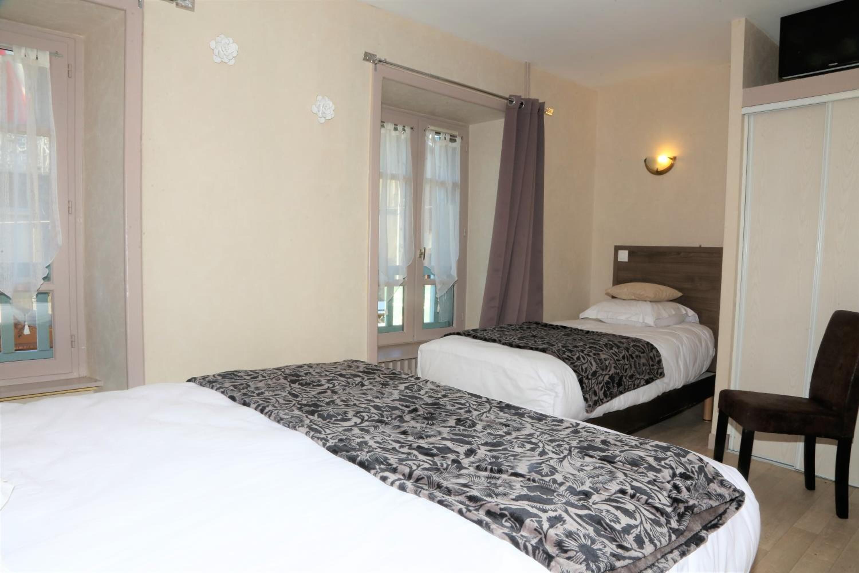 A hotel room with two beds, a chair, a TV, and a window with curtains.