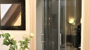 A bathroom with a glass shower enclosure, a white vanity with a vase of flowers, and a framed mirror on the wall. - Hotel Ecu de France (Mauriac)