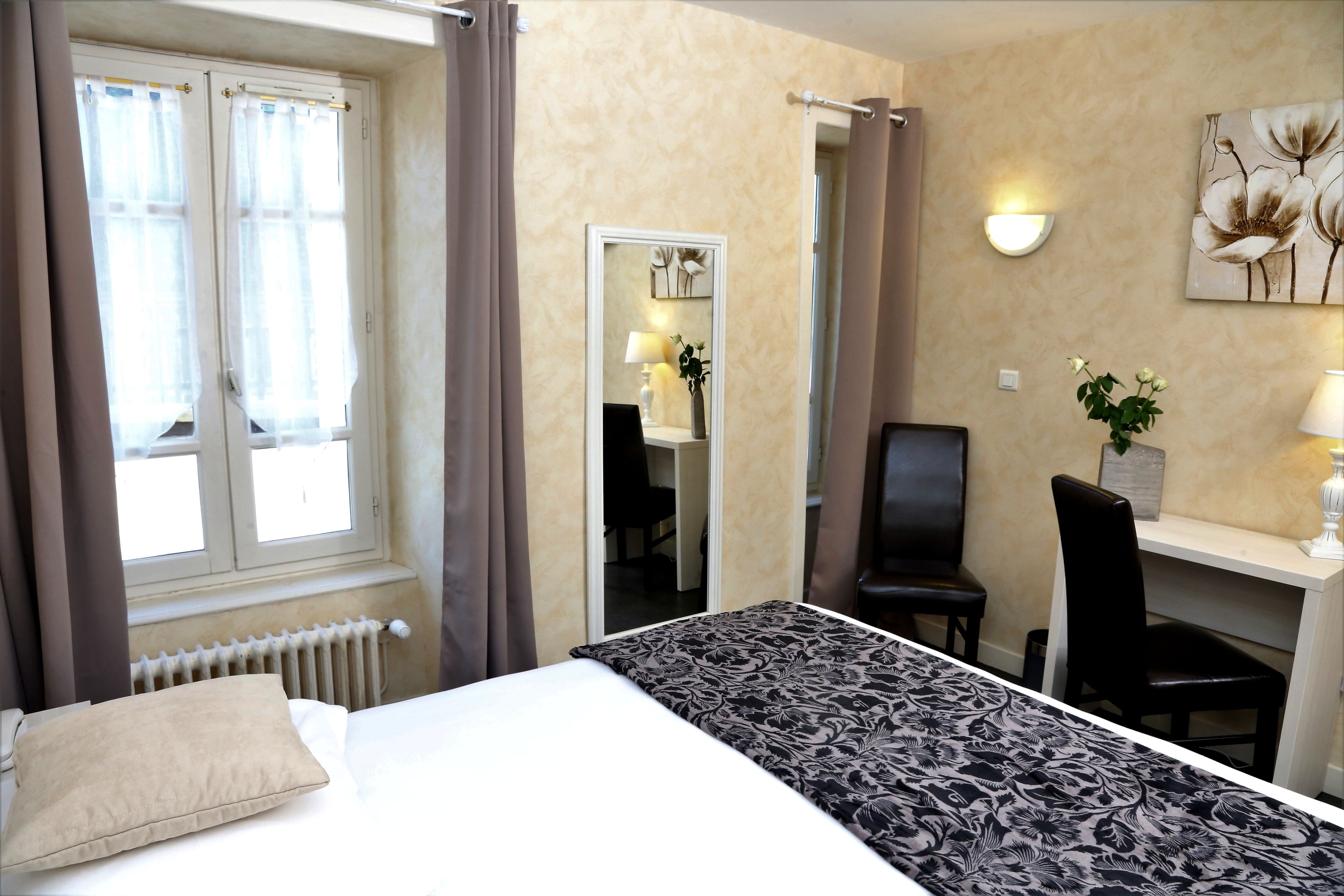 Habitación de hotel con cama, escritorio, silla, espejo y ventana con cortinas.