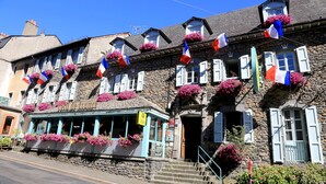 A stone building with multiple windows, some with shutters, and balconies with flowers. Flags are strung across the building. - Hotel Ecu de France (Mauriac)
