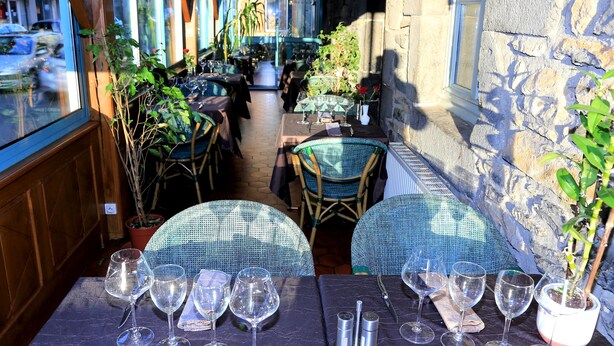 An outdoor dining area with wicker tables and chairs, potted plants, and a view of the street. - Hotel Ecu de France (Mauriac)