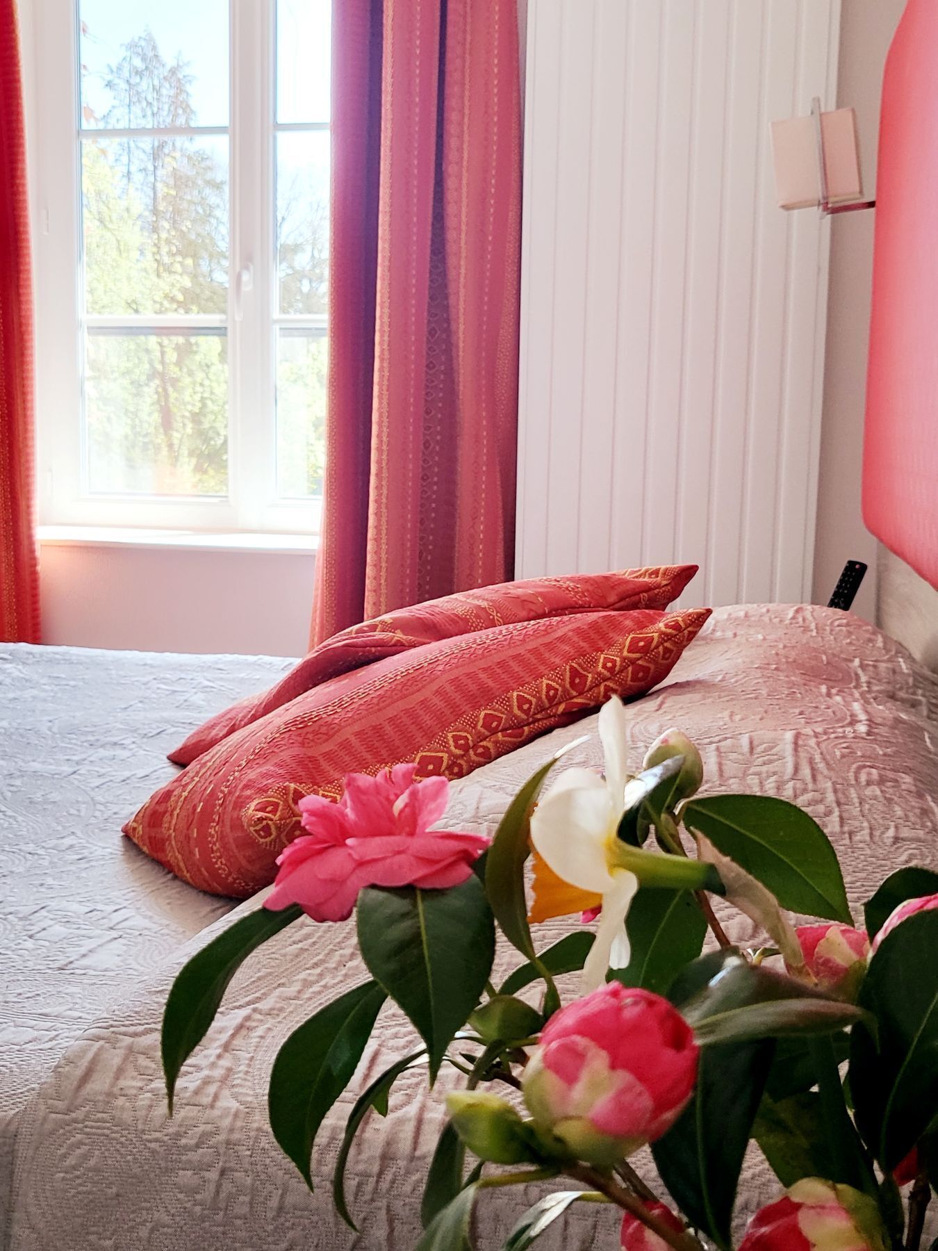 A bed with a patterned bedspread, two pillows, and a vase with flowers.