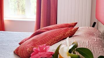 A bed with a patterned bedspread, two pillows, and a vase with flowers.