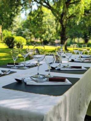 A table set outdoors with clear glassware and cutlery, surrounded by greenery. - Hôtel De France Restaurant Grill - Domfront (Domfront en Poiraie)