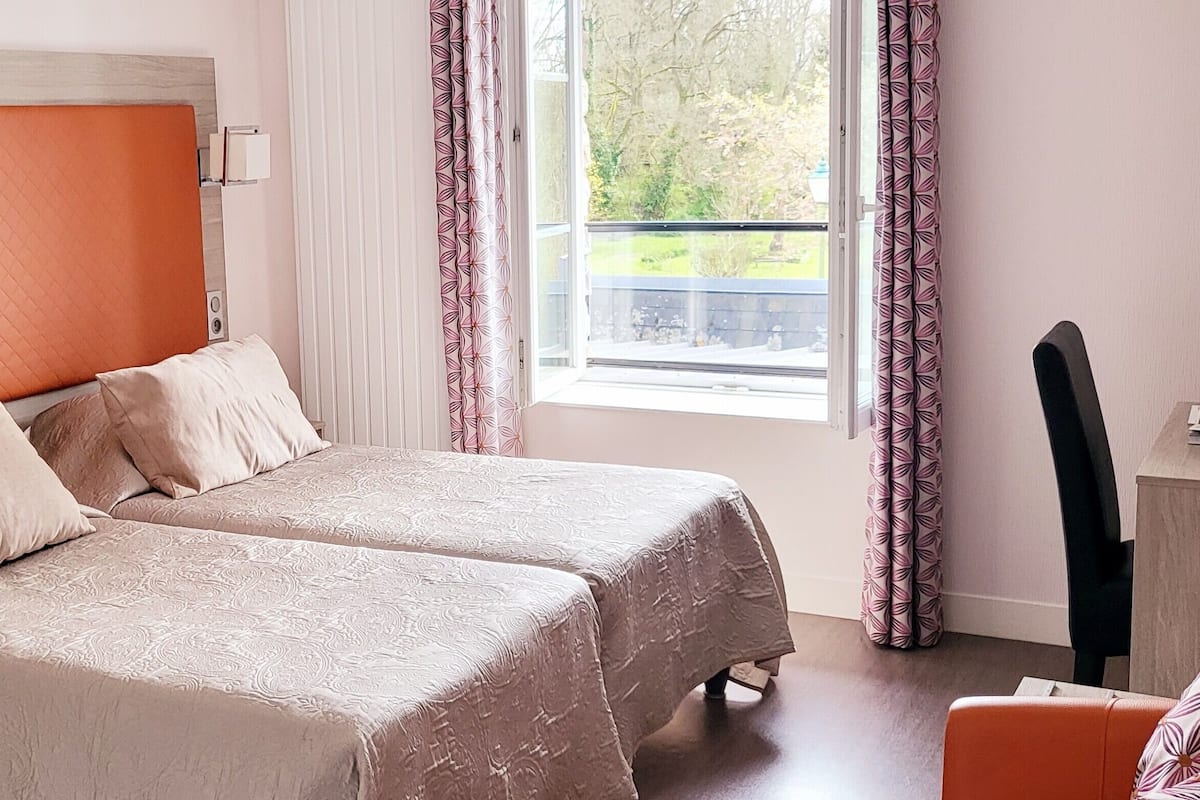A double bed with a quilted headboard, two bedside tables, a desk with a chair, and a window with curtains.
