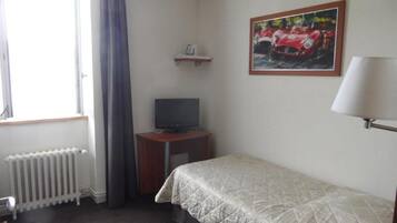 A hotel room with a bed, a television on a wooden stand, a radiator, a window with curtains, and a painting of a red car on the wall.
