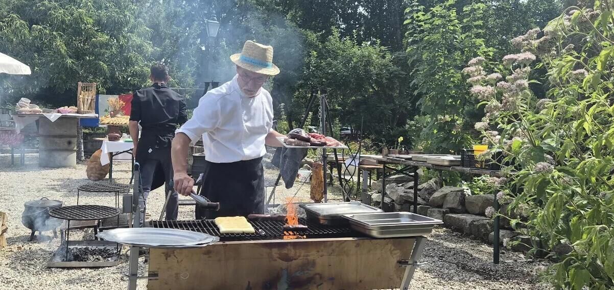 Un chef asando alimentos al aire libre, con una parrilla y utensilios de cocina.