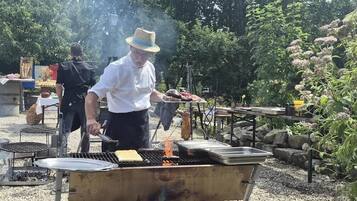 Un chef asando alimentos al aire libre, con una parrilla y utensilios de cocina.
