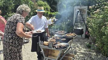 An outdoor barbecue with a grill and a portable stove, surrounded by greenery.