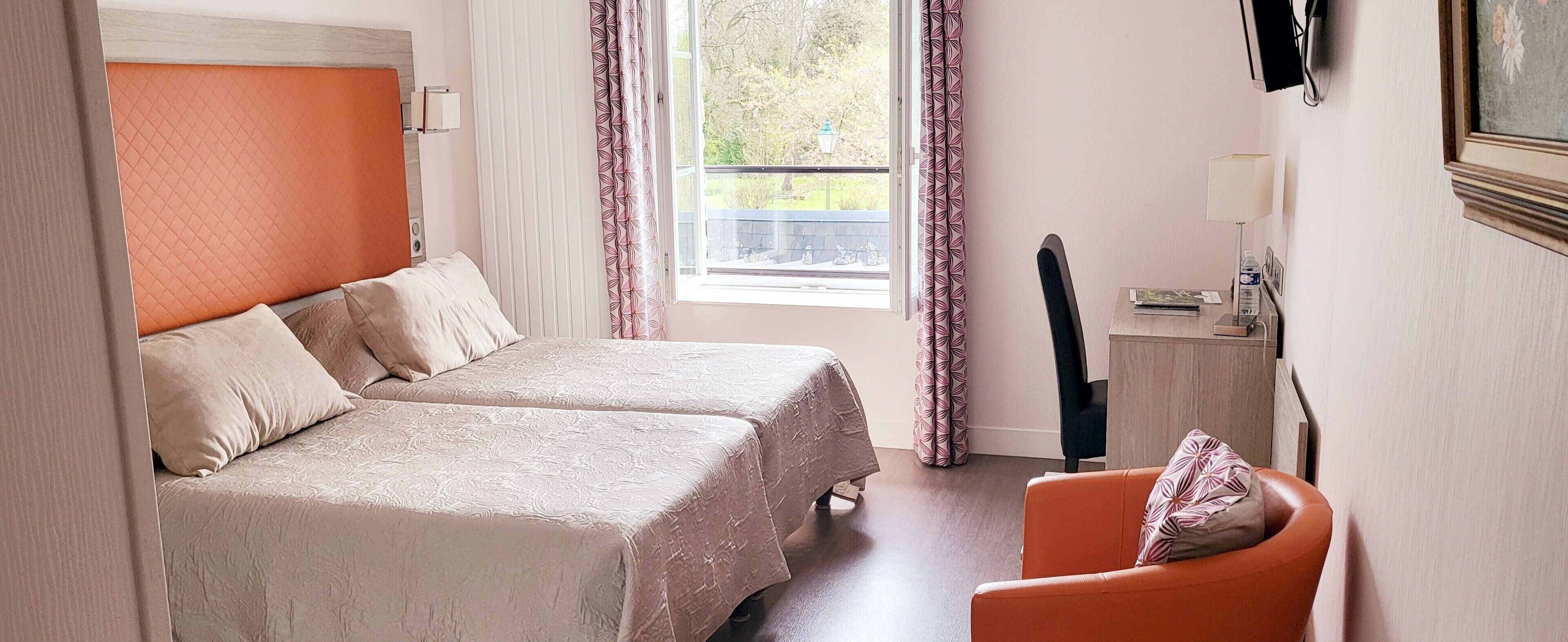 Une chambre d’hôtel avec deux lits, un bureau, une chaise, une fenêtre avec des rideaux et une vue sur l’extérieur.